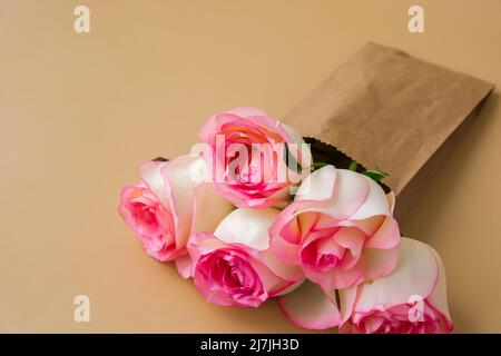 Zarte rosafarbene Rosen in einer Bastelpapiertasche auf beigem Hintergrund. Minimalistisch trendige Komposition. Abstrakte Kunstidee. Romantische rosa Rosenblüten in Pastelltönen. Moderne Ästhetik. Neutrale Erdtöne. Grußkarte Hintergrund Kopierbereich Banner Stockfoto