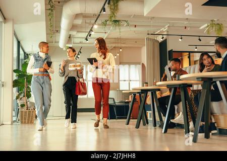 Eine Gruppe von Geschäftsfrauen, die morgens durch ein modernes Büro laufen. Drei junge Geschäftsfrauen, die eine wichtige Diskussion führen. Unternehmerinnen Stockfoto