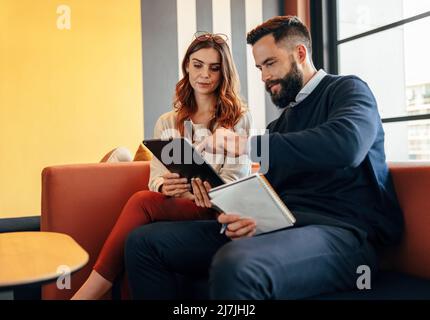 Geschäftspartner, die ein digitales Tablet in einer Bürolobby nutzen. Zwei moderne Geschäftsleute, die eine wichtige Diskussion in einem Co-Working-Raum führen. Zwei Sie Stockfoto