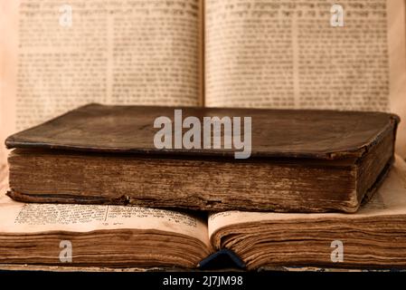 Alte abgenutzte, schäbige jüdische Bücher in Ledereinband und offene, verschwommene Tora im Hintergrund. Nahaufnahme. Selektiver Fokus Stockfoto