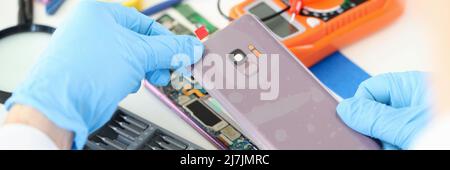 Handwerker in Gummihandschuhen, die die Abdeckung des Mobiltelefons in der Nähe der Werkstatt schließen Stockfoto