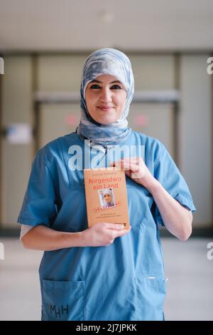 Hannover, Deutschland. 29. April 2022. Die Intensivpflegerin Farah Hareb-Demir hält das Buch „Nowhere a Country“ auf dem Campus der Medizinischen Hochschule Hannover (MHH) in der Hand. In dem Buch beschreibt die Krankenschwester ihre Geschichte zusammen mit dem Journalisten Gunnar Menkens. Hareb-Demir lebt seit mehr als 30 Jahren in Deutschland, doch trotz mehrerer Gerichtsverfahren und eines unbefristeten Arbeitsvertrages drohen die Einwanderungsbehörden ihr weiterhin mit Abschiebung. (To dpa 'unklare Identität: Intensivkrankenschwester immer noch nur toleriert') Quelle: Ole Spata/dpa/Alamy Live News Stockfoto