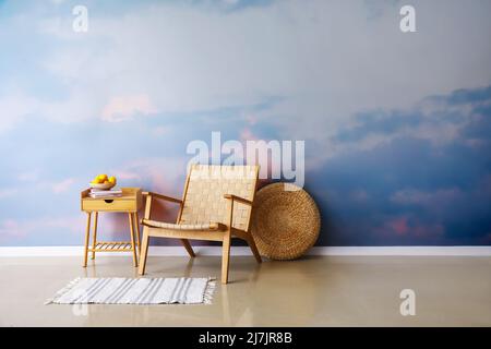 Stilvoller Rattansessel mit Teppich und Tisch neben bemalten Wänden im Zimmer Stockfoto