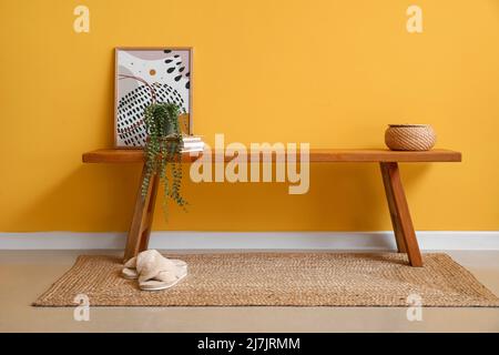 Holzbank mit Bild, Büchern und Zimmerpflanze in der Nähe der gelben Wand Stockfoto