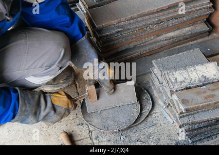 Arbeiter in der Schwerindustrie oder Metallurgie schlagen Eisenplatten mit Hammer ab. Arbeiten Sie mit Metall. Beschaffung von Wertstoffen für die Produktion. Authentischer Workflow. Stockfoto