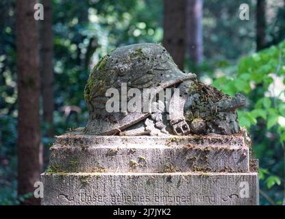 Stahnsdorf, Deutschland. 02.. Mai 2022. Ein mit Lorbeerkranz besetzter Helm aus Stein auf einem Grabstein mit der Aufschrift „Unser geliebtes einziges Kind“, fotografiert auf dem Südwestkirchhof der Berliner Stadtsynode. Der Friedhof südwestlich von Berlin ist mit einer Fläche von über 200 Hektar der zweitgrößte in Deutschland. Aufgrund seines Waldcharakters und seiner vielen historischen Grabstätten ist der Südwestkirchhof ein beliebtes Touristenziel. Für die Erhaltung des kulturell und kunsthistorisch bedeutsamen Ortes wurde 2000 ein Förderverein gegründet. Quelle: Soeren Stache/dpa/ZB/dpa/Alamy Live News Stockfoto