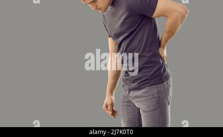 Junger Mann, der unter Rückenschmerzen aufgrund großer körperlicher Anstrengung leidet, isoliert auf grauem Hintergrund. Stockfoto