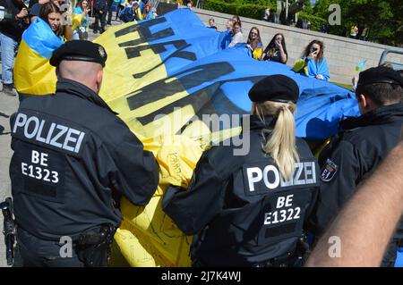 Am 8. Mai 2022 rollt die Polizei eine riesige ukrainische Flagge auf, die von den Demonstranten am sowjetischen Kriegsdenkmal in Tiergarten, im Zentrum von Berlin, gezeigt wird. Stockfoto