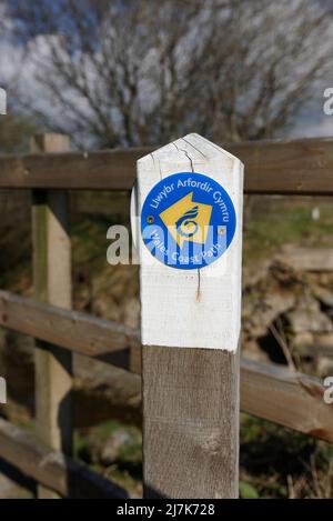 Zweisprachiger hölzerner waliser und englischer walisischer Küstenpfad, Schild, öffentliches Verkehrsrecht, mit Holzzaun im Hintergrund in der Landschaft von nordwales, großbritannien Stockfoto