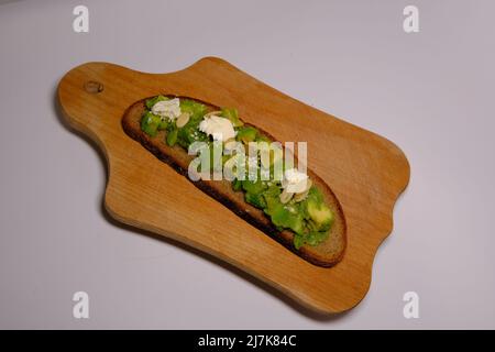 Gesunder hausgemachter Avocado cremiger Toast aus grauem Brot mit Kleie mit Kürbiskernen und cremigem Käse auf Holzbrett auf isoliertem Hintergrund. In t Stockfoto