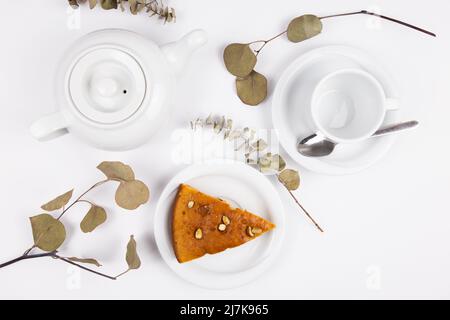 Stück Kuchen auf einer Untertasse mit einer Tasse Tee oder Kaffee und einem Wasserkocher Stockfoto