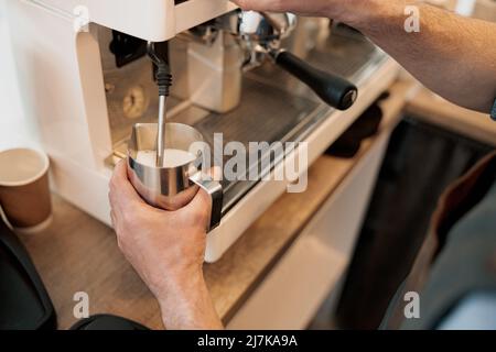 Nahaufnahme von Barista-Händen, die Milch im Krug mit Dampf aufheizen Stockfoto