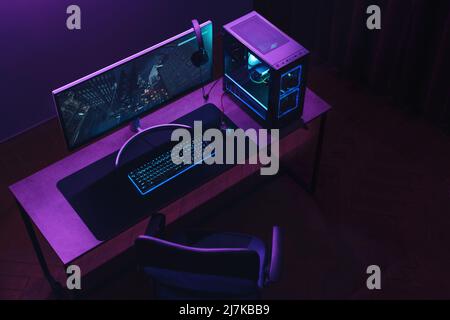 Draufsicht auf den Arbeitsbereich der Gamer und die professionelle Gaming-Einrichtung: Maus, Tastatur, Monitor, Headset, leistungsstarker Computer. Premium-PC mit RGB-Licht im Inneren. Cyber-Sportler leeres Studio mit Streaming-Setup Stockfoto