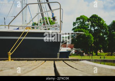 Blick auf das Segelboot, das an einem hölzernen Steg im Hafen festgemacht ist, Nahaufnahme des Rumpfes und Bogens des Segelbootes Stockfoto