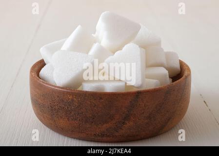 Brückenförmige Zuckerwürfel in Holzschüssel auf weißem Holzhintergrund. Nahaufnahme aus dem unteren Winkel, keine Personen. Stockfoto