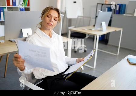 Geschäftsfrau, die Dokumente am Schreibtisch im Büro prüft. Büroangestellter, der Papierkram macht Stockfoto