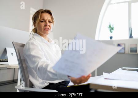 Unzufriedene Geschäftsfrau prüft Dokumente an ihrem Arbeitsplatz im Büro Stockfoto