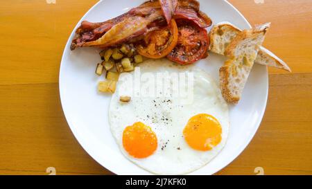 Amerikanisches Frühstück mit Spiegeleiern auf der sonnigen Seite auf einem Holztisch im Restaurant Stockfoto