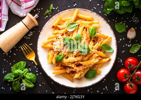 Italienische Pasta mit Tomatensauce, Basilikum und Parmesankäse auf dunklem Tisch. Stockfoto