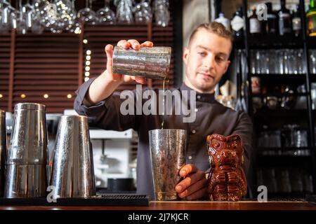 Crop konzentrierte junge männliche Barkeeper mischen Getränke in Shaker während der Zubereitung von köstlichen Cocktail an der Theke im Restaurant Stockfoto