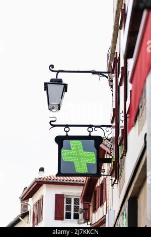 Von unten neongrünes Kreuzschild und altmodische Laterne, die vor der Drogerie am grauen Himmel in der Stadt hängt Stockfoto