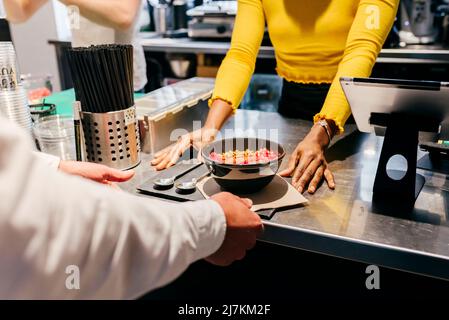 Crop African American Kellnerin geben Tablett mit Smoothie Schüssel und Löffel dienen Kunden über der Theke in einem kleinen Café Stockfoto