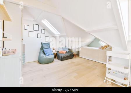 Komfortables Bett mit Kissen und Decke auf leichter Mansarde mit Sitzkissen in der Wohnung platziert Stockfoto