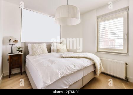 Komfortables Bett mit Pelzdecke und Kissen in hellen geräumig mit Fenstern platziert Stockfoto