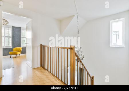 Hölzerne Treppengeländer in geräumigen Korridor führt zum Zimmer mit komfortablen gelben Sessel in modernen Haus bei Tageslicht Stockfoto