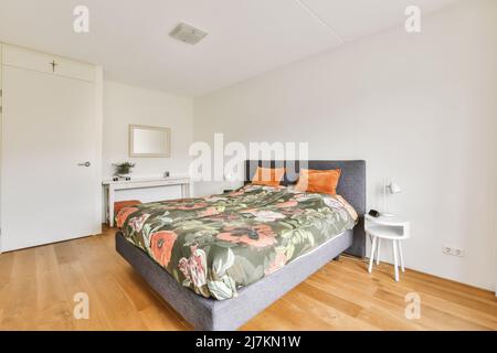 Komfortables Bett mit farbenfroher Decke und Kissen in hellem, geräumigen Schlafzimmer zu Hause Stockfoto