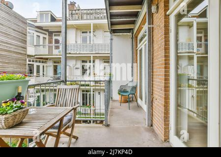 Stuhl und Tisch mit Flasche und Brille in der Nähe von Metallzaun auf dem Balkon mit Blick auf Gebäude in der Stadt am Sommertag Stockfoto