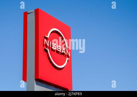 Minsk, Weißrussland - 10. Mai 2022: Nissan. Eine rote Plakatwand mit dem Nissan-Logo auf einem blauen Himmel Hintergrund. Stockfoto