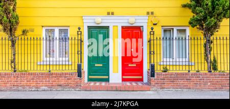 Fassade eines gelben Wohnhauses mit Fenstern und bunten Türen in der Nähe von Metallzaun und Gehweg auf der Straße der Stadt Stockfoto