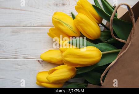 Strauß gelber Tulpen in einem Kraftpapier-Beutel auf weißem Holzhintergrund Stockfoto