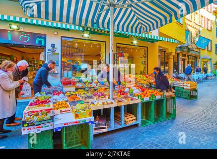 LUGANO, SCHWEIZ - 25. MÄRZ 2022: Der große Obststand mit frischen Orangen, Äpfeln, Kiwi, Granatäpfeln und anderen Früchten in der schmalen Via Pessina, ON Stockfoto