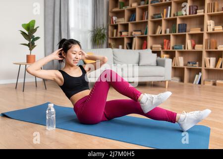 Sport zu Hause Konzept. Fit asiatische Frau in Sportbekleidung Training auf Fitness-Matte, tun knirscht, arbeiten an abs Stockfoto