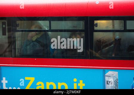 Passagiere, einige tragen eine Maske, andere nicht, werden in einem Doppeldeckerbus in der City of London gesehen. Stockfoto