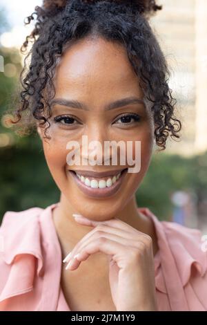 Nahaufnahme des Porträts einer lächelnden afroamerikanischen Geschäftsfrau mit mittlerem Erwachsenenalter mit der Hand am Kinn Stockfoto