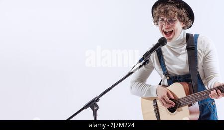 Porträt eines jungen Emotiona-Mannes, Musiker, der akustische Gitarre spielt und singt. Konzept von Kunst, Musik, Stil und Kreation Stockfoto