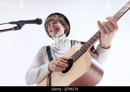 Porträt eines jungen Emotiona-Mannes, Musiker, der akustische Gitarre spielt und singt. Konzept von Kunst, Musik, Stil und Kreation Stockfoto