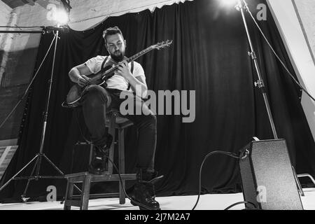 Wiederholung der Retro-Musikband im Musikstudio. Junger Musiker, der E-Gitarre spielt und singt. Probenbasis. Konzept von Kunst, Musik, Stil und Stockfoto
