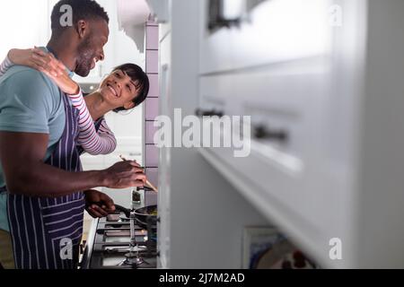 Lächelndes, multirassisches junges Paar, das zu Hause gemeinsam Essen kocht Stockfoto