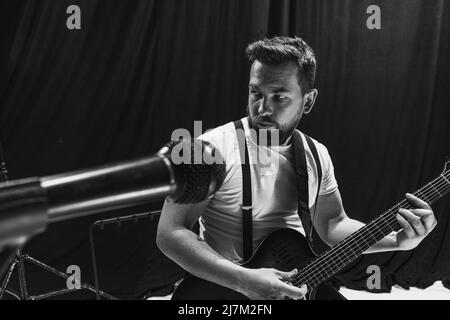 Wiederholung der Retro-Musikband im Musikstudio. Junger Musiker, der E-Gitarre spielt und singt. Probenbasis. Konzept von Kunst, Musik, Stil und Stockfoto