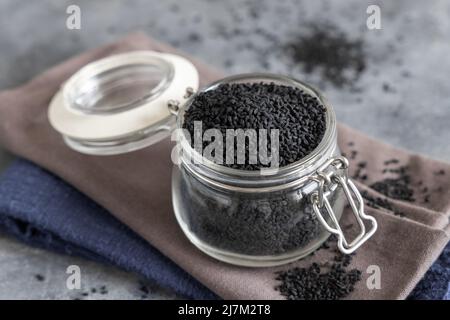 Indische Gewürz Schwarzer Kreuzkümmel (Nigella sativa oder Kalonji) Samen Glas auf grauem Tisch Nahaufnahme mit Kopierraum Stockfoto