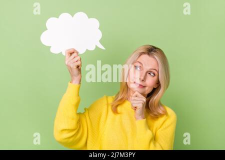 Foto von nachdenklichen interessierten alten Dame halten Papier Rede Wolke erwägen isoliert grüne Farbe Hintergrund Stockfoto