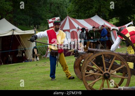 Männer und Frauen feuern während einer Nachstellung einer mittelalterlichen Schlacht Musketen und Holzkanonen Stockfoto