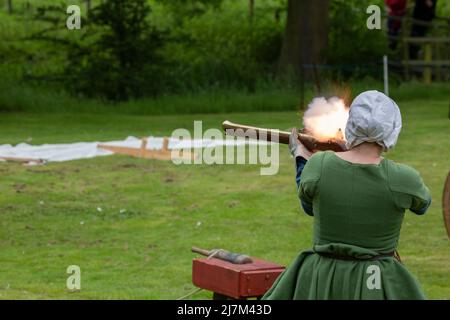 Männer und Frauen feuern während einer Nachstellung einer mittelalterlichen Schlacht Musketen und Holzkanonen Stockfoto