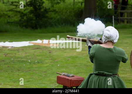 Männer und Frauen feuern während einer Nachstellung einer mittelalterlichen Schlacht Musketen und Holzkanonen Stockfoto