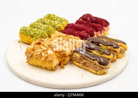 Eclair-Kuchen. Auswahl an Eclare-Kuchen auf weißem Hintergrund. Schokolade, Pistazie, Himbeer-eclair-Kuchen auf Marmorstein Stockfoto