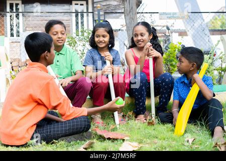 Fröhliche Teenager-Kinder, die sich nach dem Cricket-Spielen im Park unterhalten - Konzept der Pause, Freundschaft und Geselligkeit. Stockfoto